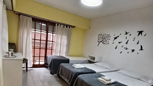 Ein Zimmer mit drei Betten, einem Schreibtisch und einem Fenster mit Vorhängen.