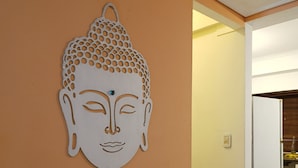 Ein Flur mit einer an der Wand befestigten Buddha-Kopf-Skulptur, einer weißen Tür und einem gefliesten Boden.