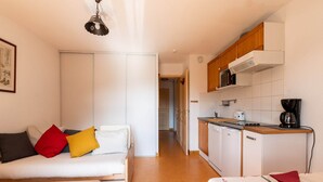 A compact living space with a kitchenette, a sofa with colorful cushions, and a dining area.