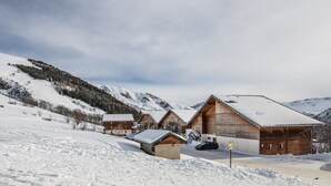 A snow-covered mountain lodge with wooden cabins, a parking area, and a clear view of the surrounding mountains.