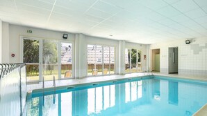 A swimming pool with clear glass walls, a tiled floor, and a view of outdoor seating.