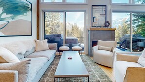 A modern living room with a sofa, armchair, and coffee table, large windows with a mountain view, and a fireplace. - Luxury Lodge w/ Breathtaking Mountain Views, large yard, fireplace  & WIFI (Snoqualmie Pass)