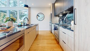 A modern kitchen with a large island, wooden cabinets, and a view of the outdoors through large windows. - Luxury Lodge w/ Breathtaking Mountain Views, large yard, fireplace  & WIFI (Snoqualmie Pass)