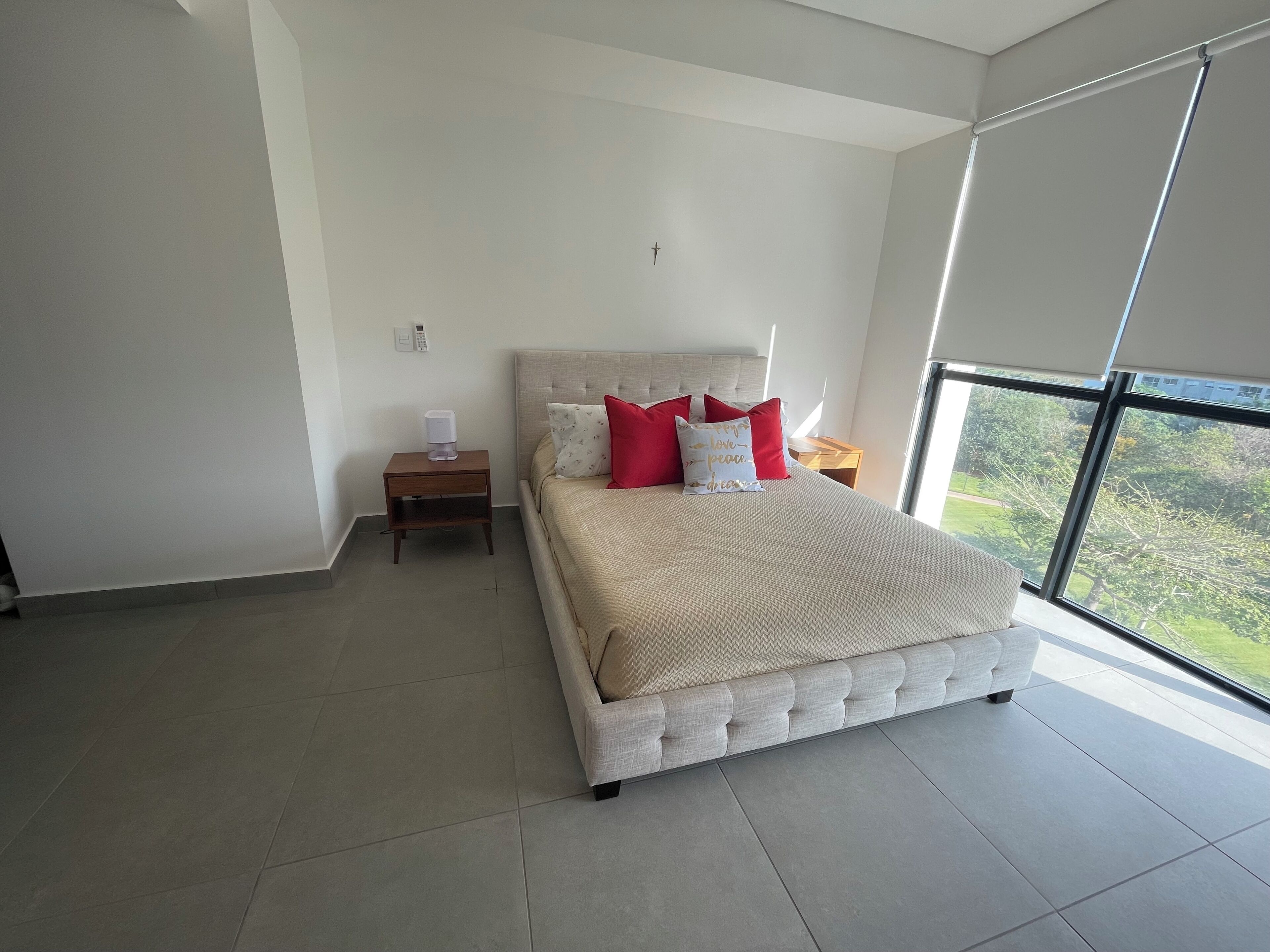 Een moderne slaapkamer met een groot bed, nachtkastje en een uitzicht op groen door grote ramen.