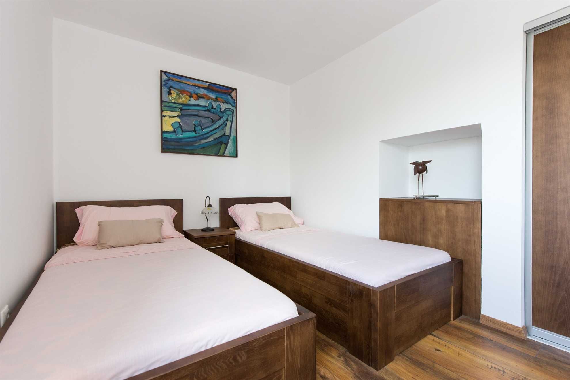 A bedroom with two beds, a nightstand, a lamp, and a painting on the wall.