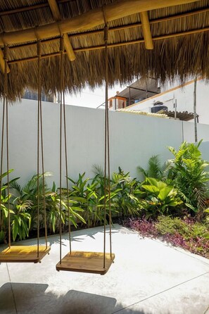 A thatched-roof outdoor area with two wooden swings, surrounded by lush greenery and a white wall. - Warm Haven in Puerto Vallarta 2 Bedrooms (Puerto Vallarta)