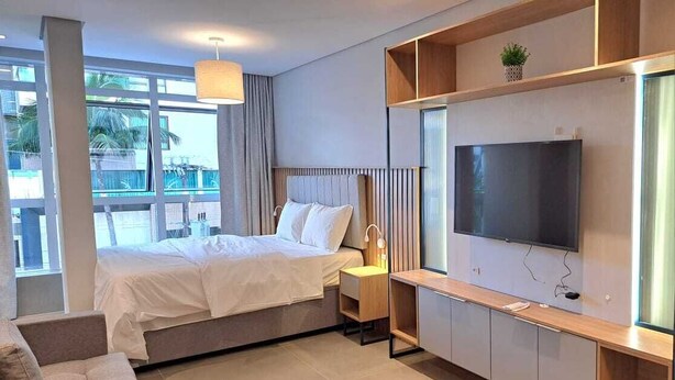 A modern hotel room with a bed, a TV, a sofa, and a balcony with a view of palm trees. - Beautiful Studio 200m from Beira Mar, Center of Florianópolis! (Centro Florianópolis)