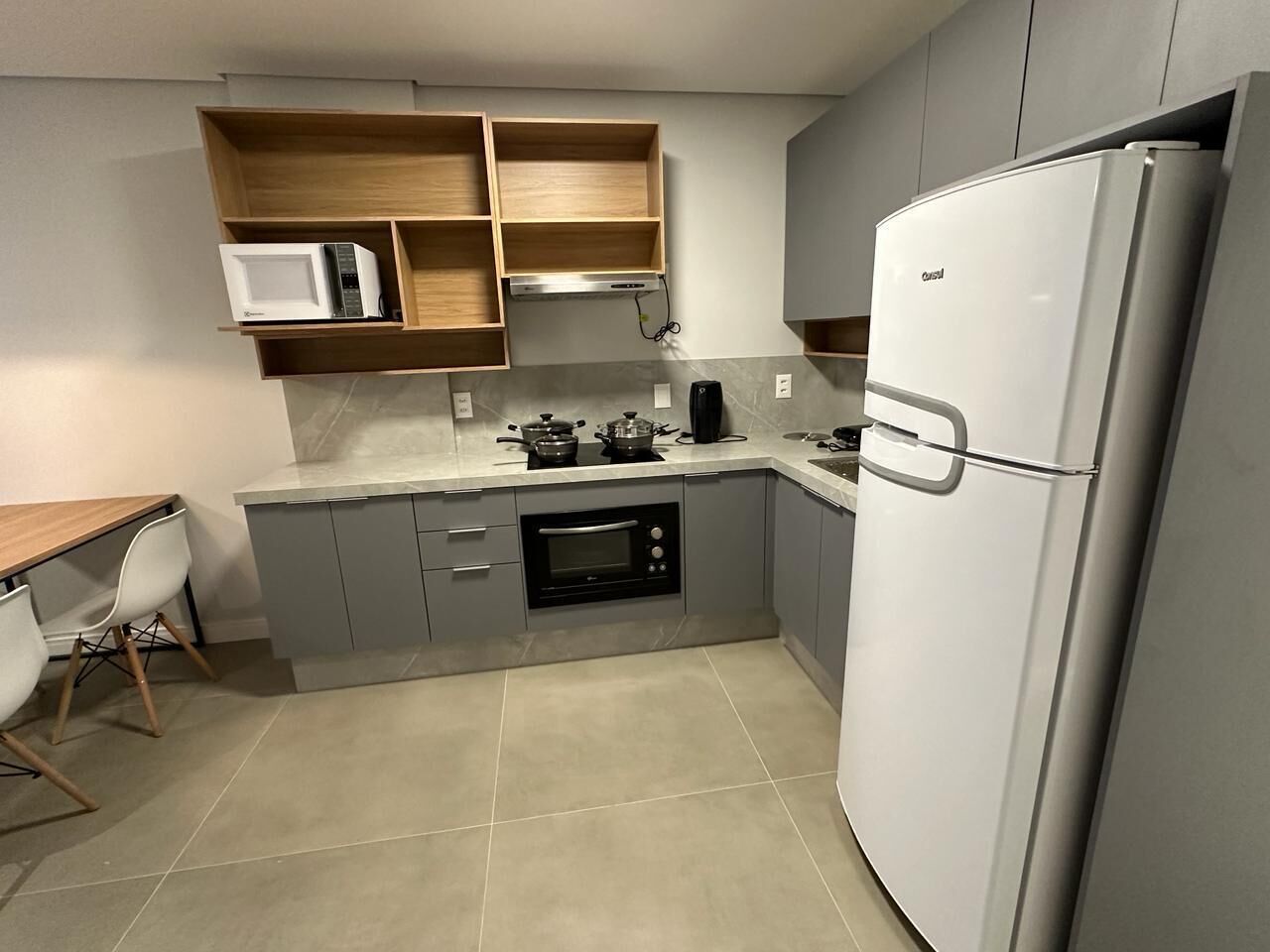 Cocina compacta con armarios grises, un refrigerador blanco, un microondas y un horno empotrado.