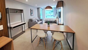 A modern, well-lit room with a wooden dining table, two white chairs, a grey sofa, and a small potted plant. - Beautiful Studio 200m from Beira Mar, Center of Florianópolis! (Centro Florianópolis)