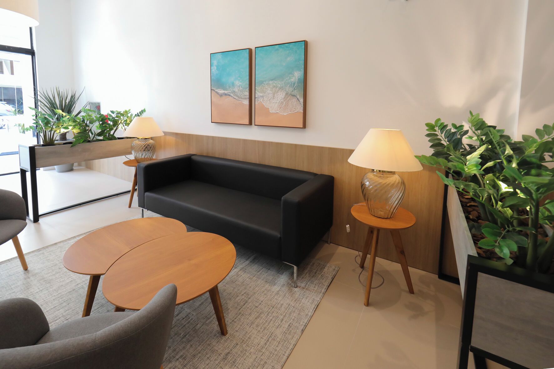 En modern entréhall med en svart soffa, två träbord och krukväxter.