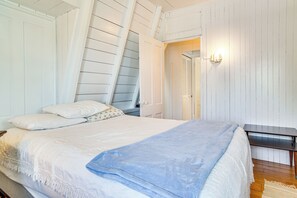 A bedroom with a bed, a nightstand, a desk, and a wall-mounted light fixture.