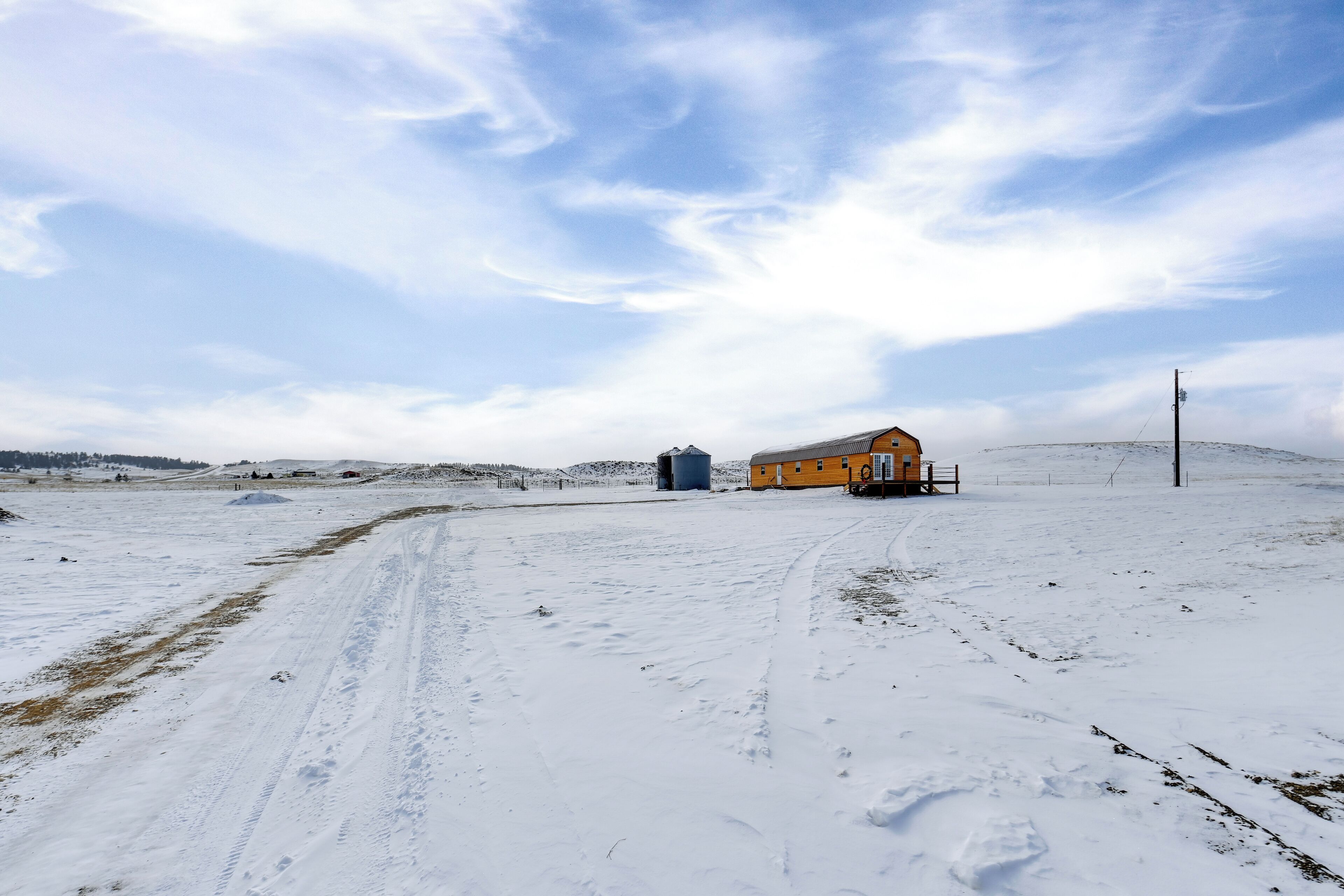 Paisaje nevado con un edificio amarillo, un silo y una línea de electricidad.