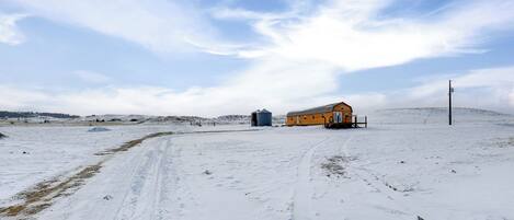 Paisaje nevado con un edificio amarillo, un silo y una línea de electricidad.