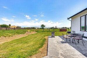 Eine Terrasse mit Tisch und Stühlen, einem Steingartenbeet und Blick auf ein Wiesfeld und Hügel im Hintergrund.