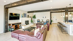 A spacious living room with a large leather sofa, a flat-screen TV, and a fireplace. There is a kitchen area with bar stools and pendant lighting. - Fish, Boat & Unwind: Old Hickory Lake Retreat (Mt. Juliet)