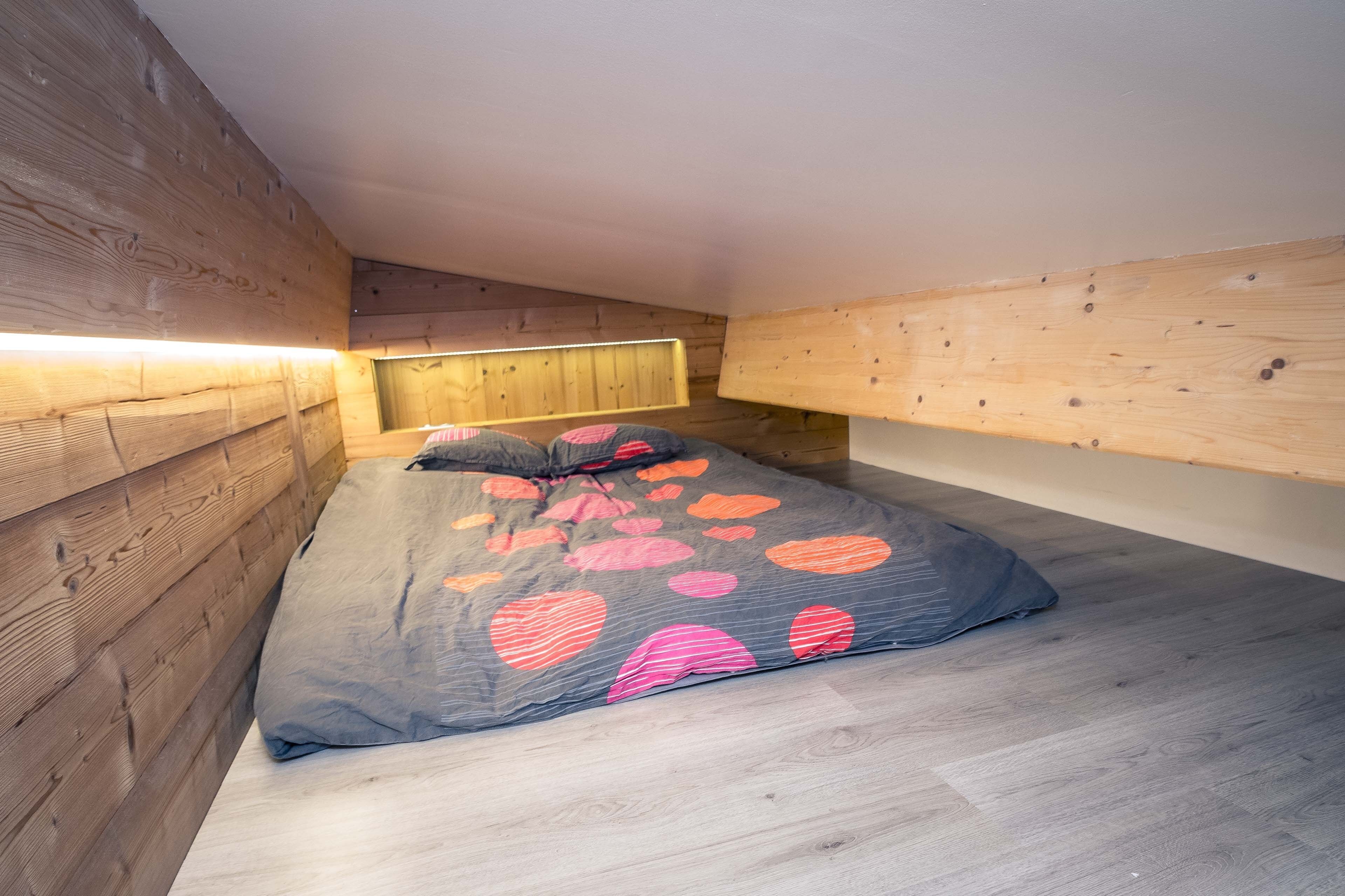 Une petite pièce chaleureuse, avec un lit, des murs en bois et un plafond en pente.