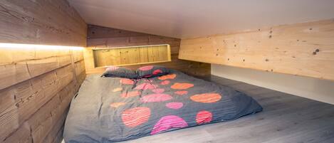 Une petite pièce chaleureuse, avec un lit, des murs en bois et un plafond en pente.
