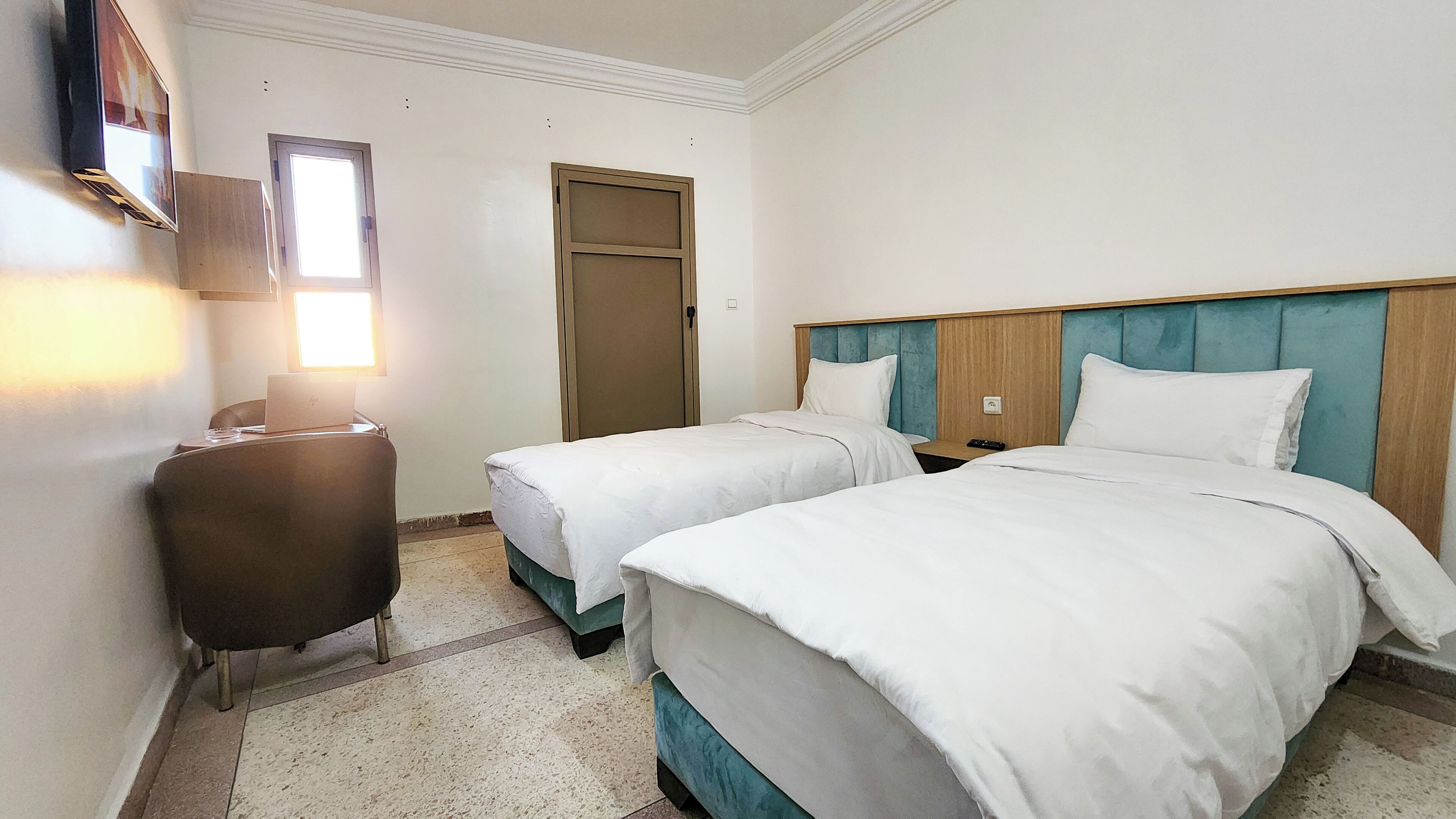 A hotel room with two single beds, a desk with a chair, a TV mounted on the wall, and a door.