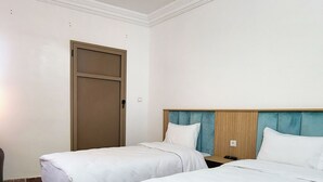 A hotel room with two beds, a wooden headboard, a door, and a tiled floor. - Hotel nakhil dak (Dakhla)