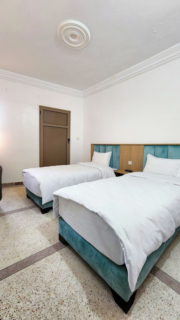 Habitación de hotel con dos camas, cabecero de madera, una puerta y suelo de baldosas.