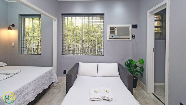 A modern bedroom with a bed, two windows, an air conditioning unit, and a potted plant. - Pompeu Loureiro (Rio de Janeiro)