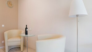 Ein modernes Zimmer mit einem weißen, bogenförmigen Sessel, einem kleinen Glastisch mit Flasche und Gläsern sowie einer hohen Stehlampe.