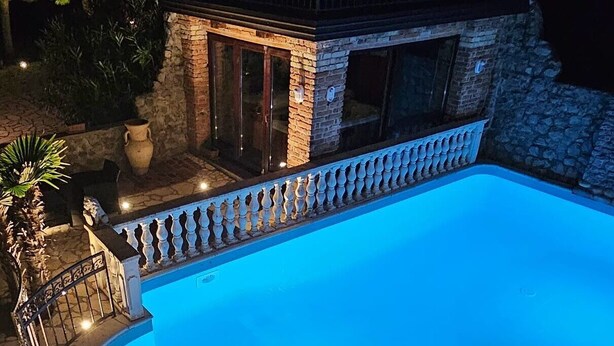 A swimming pool with a stone wall and a balustrade, surrounded by a stone patio and potted plants. - Casa Oasa  (Koper)