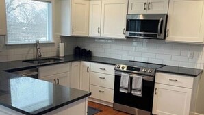 Una cocina con armarios blancos, horno de acero inoxidable y encimera negra.