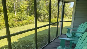 A covered porch with wooden flooring and green Adirondack chairs. - Cozy 2-bedroom townhome with AC, WiFi walk to Orange Beach (Orange Beach)