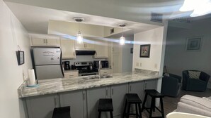 A modern kitchen with a central island, bar stools, and a dining area with a white table and chairs. - Cozy 2-bedroom townhome with AC, WiFi walk to Orange Beach (Orange Beach)