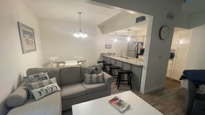A modern living room with a sofa, a coffee table, and a dining area with chairs. - Cozy 2-bedroom townhome with AC, WiFi walk to Orange Beach (Orange Beach)