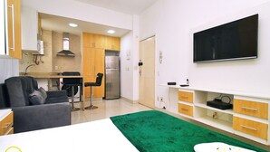 Una habitación de hotel moderna con una cama, un tapete verde, un televisor montado en la pared y una kitchenette al fondo.