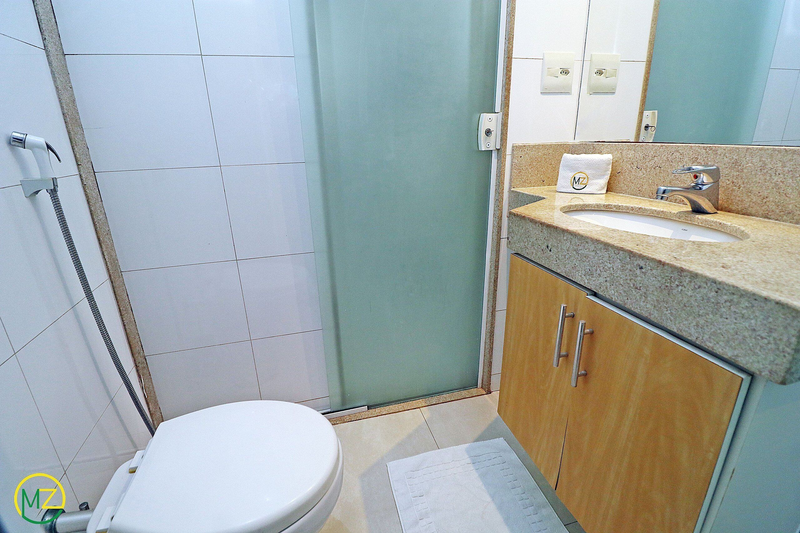 A bathroom with a toilet, shower, sink, and wooden cabinets.