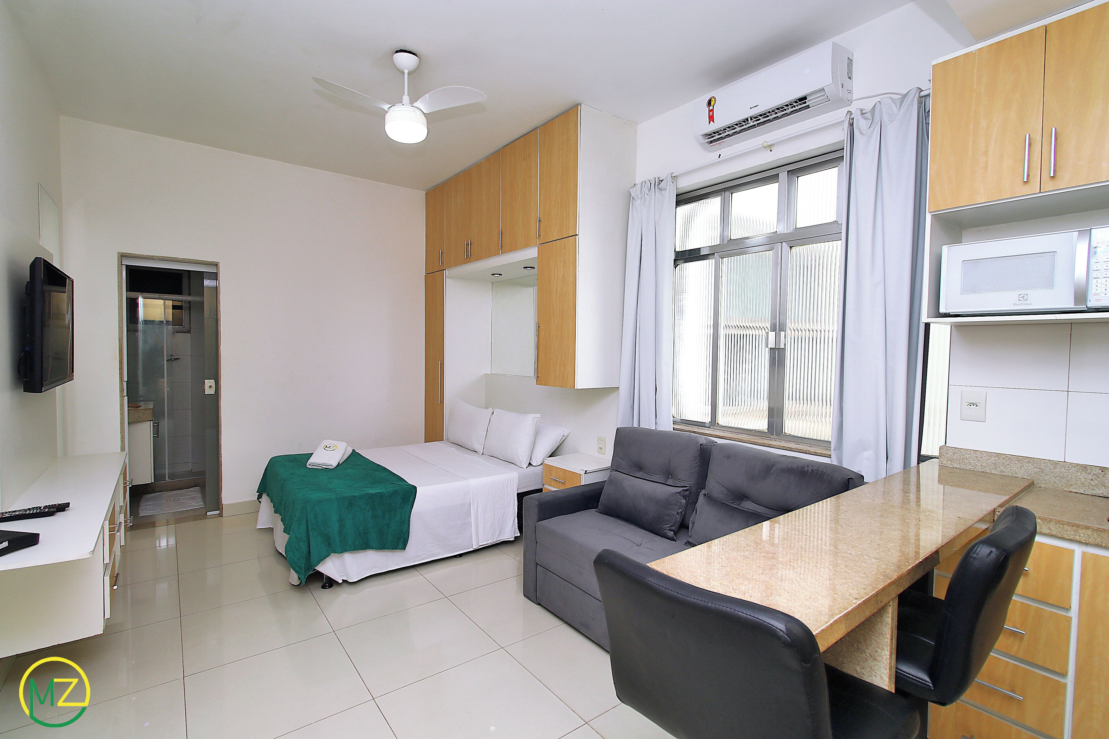 A hotel room with a bed, a sofa, a desk, a TV, and a window with curtains.