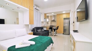 Una habitación de hotel con cama, manta verde, televisor, kitchenette y baño.