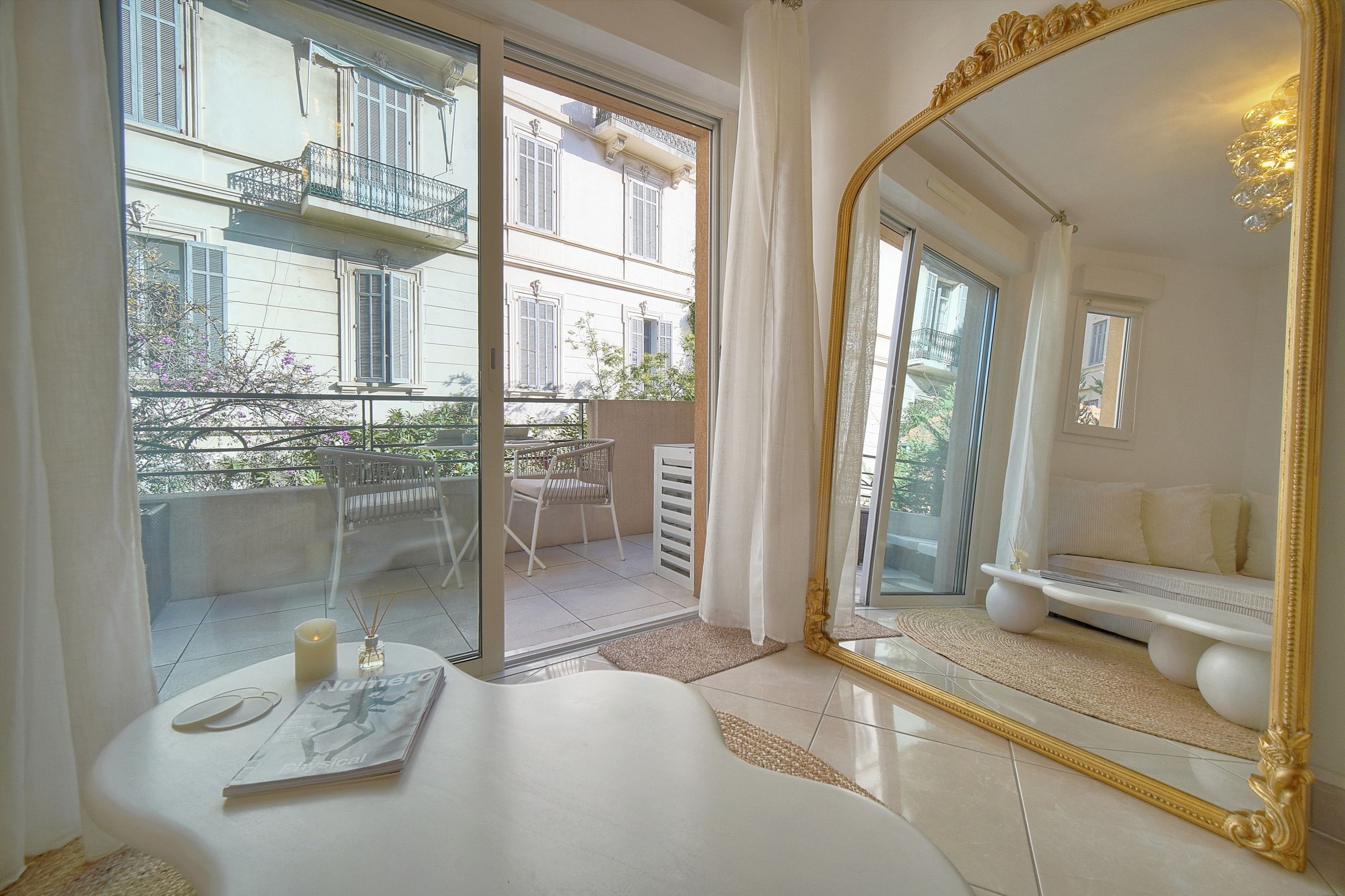 A hotel room with a large mirror, a bed, a small table with a candle and a magazine, and a balcony with a chair and a table.
