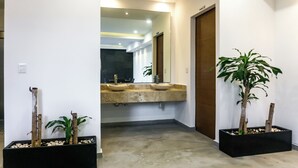Un pasillo con un lavamanos doble, dos plantas en macetas, una puerta y un interruptor de luz en la pared.