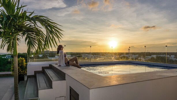 Una piscina en la azotea con vista al atardecer, una palmera y una persona relajándose.
