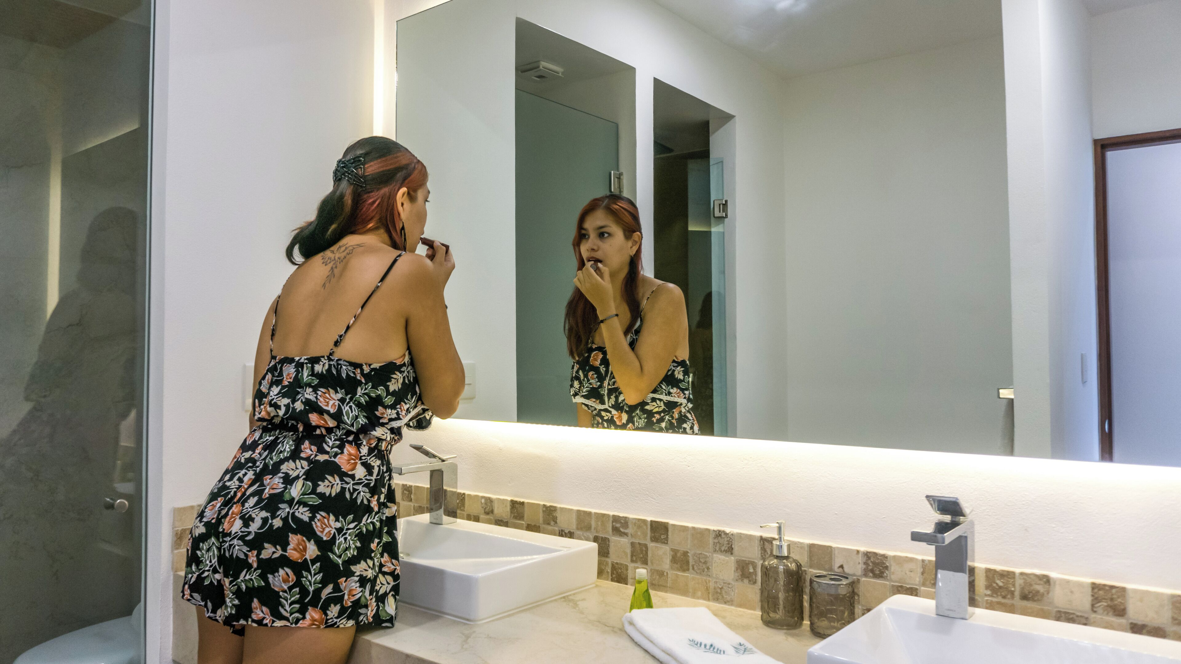 Una mujer con un vestido floral parada frente a un espejo de baño.