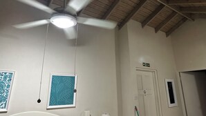 A room with a ceiling fan, a light fixture, framed artwork, a door with a no-smoking sign, and a small window. - Villa Mia Apartment Studio #4 (Oistins)