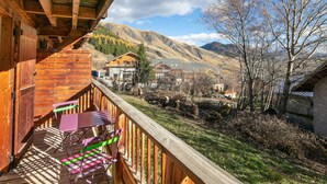 A wooden deck with a table and chairs, overlooking a mountainous landscape with buildings. - Apartment in Saint-Sorlin near Ski Resort (Saint-Sorlin-d´Arves)