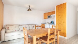 A compact living space with a wooden dining table and chairs, a sofa with patterned cushions, a kitchenette with a microwave, and a wooden door. - Apartment in Saint-Sorlin near Ski Resort (Saint-Sorlin-d´Arves)