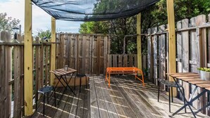 Una terraza de madera con una mesa y sillas, rodeada por una valla de madera y un toldo.
