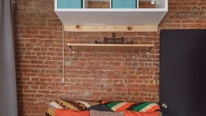 Una habitación acogedora con una pared de ladrillo, un sofá gris con cojines coloridos, una mesa blanca y una estantería sobre el sofá.