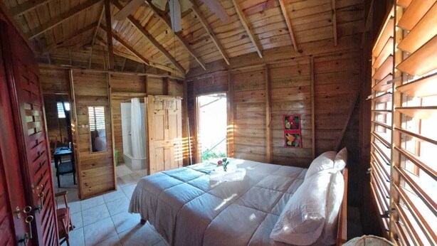 Un dormitorio de cabaña de madera con una cama, un ventilador de techo y una ventana con persianas.