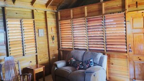 Una habitación acogedora con techo de madera, ventilador de techo, un sofá, una silla de madera, una mesita y una puerta.