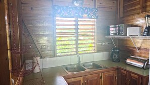 Una cocina con armarios de madera, un lavamanos doble, un microondas, una cafetera y cestas rojas colgadas.