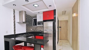 A modern kitchen with a black countertop, red bar stools, stainless steel appliances, and a tiled backsplash. - Prado X (Rio de Janeiro)