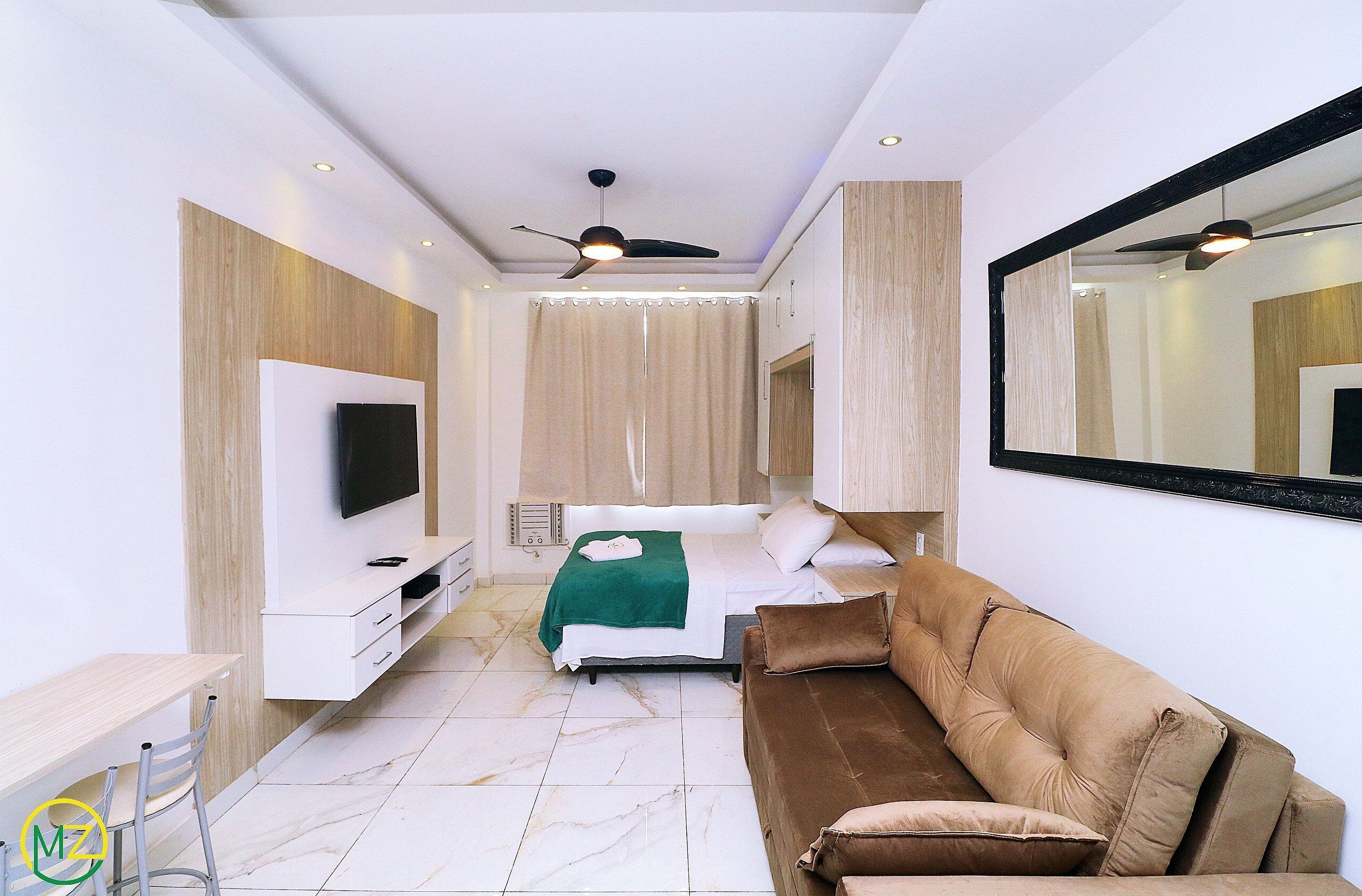 A modern bedroom with a bed, a TV, a sofa, and a large mirror.