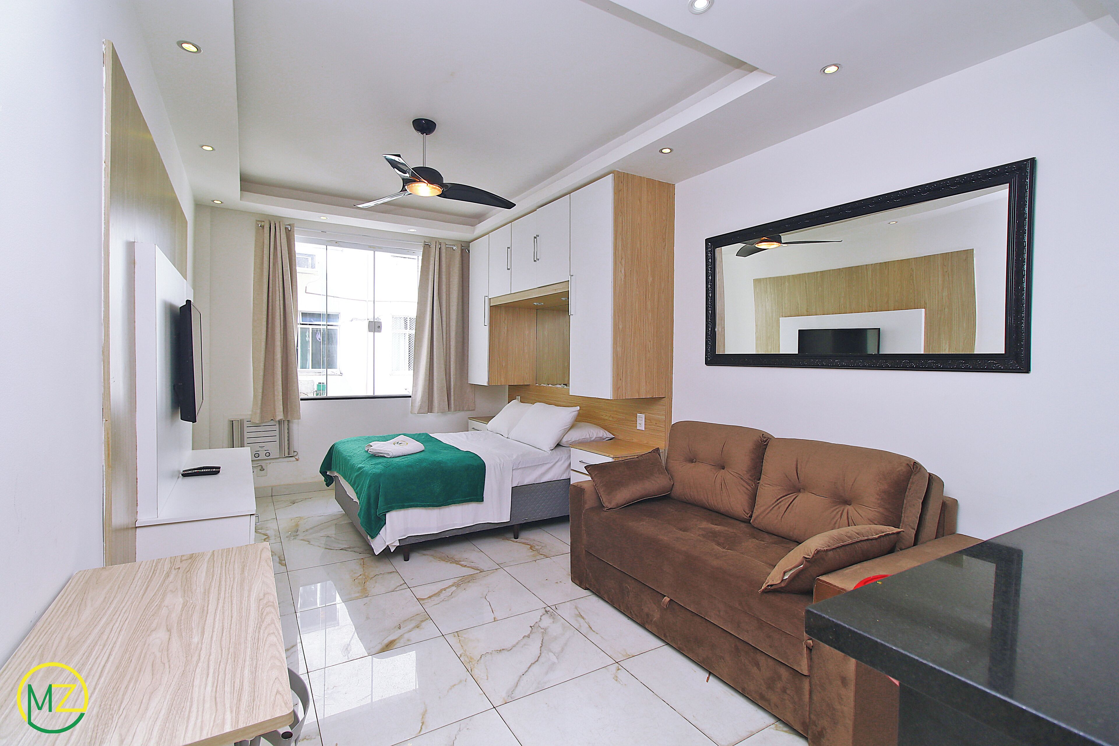 A modern hotel room with a bed, a sofa, a TV, and a ceiling fan.